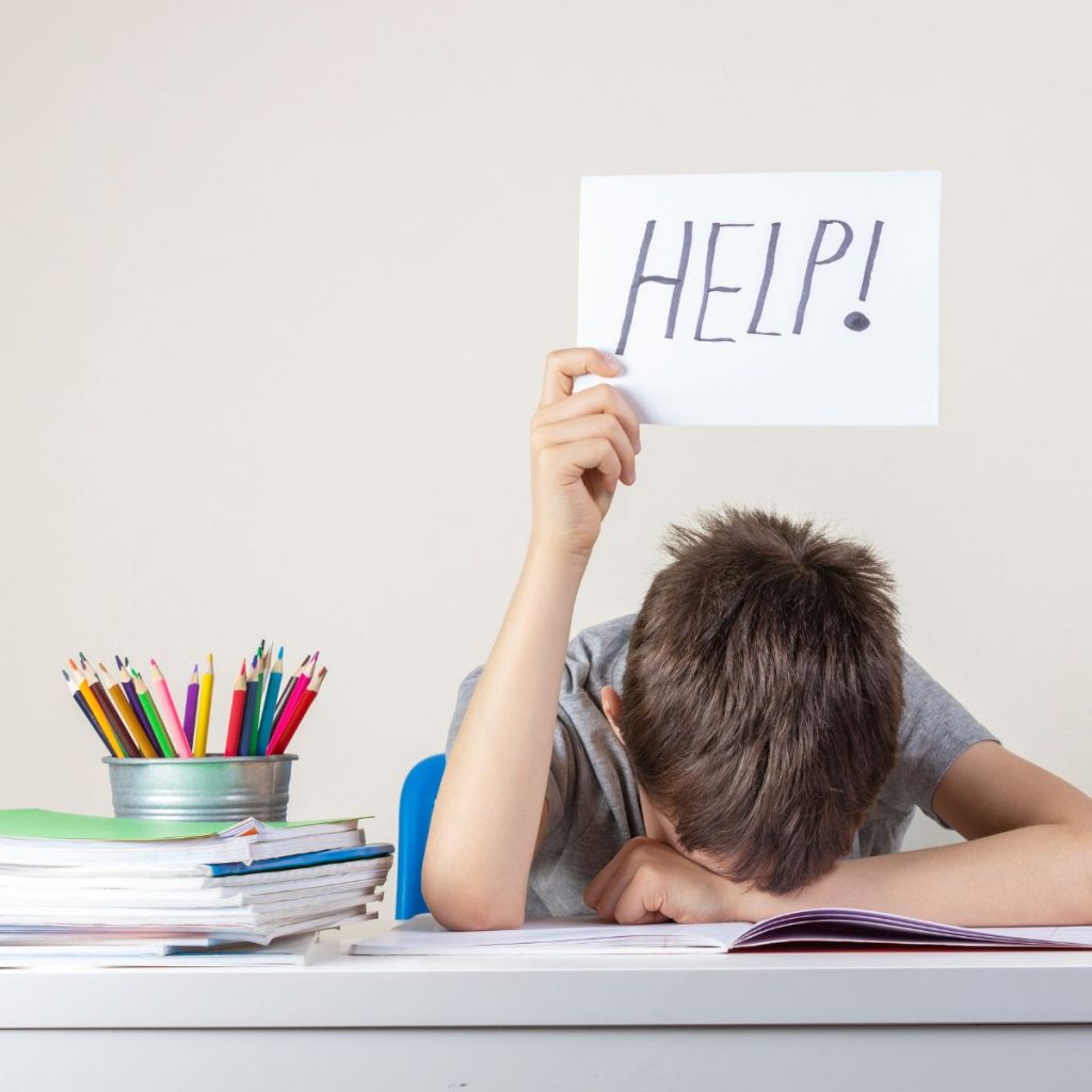 a struggling reader with his head on a desk is holding up a help sign